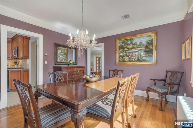 dining space with baseboards, visible vents, light wood-style flooring, ornamental molding, and a notable chandelier