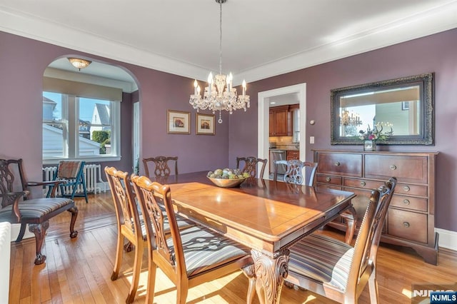 dining space with radiator, crown molding, a chandelier, light wood-style flooring, and arched walkways