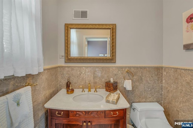 bathroom featuring vanity, visible vents, wainscoting, tile walls, and toilet