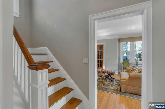 staircase with wood finished floors, baseboards, and ornamental molding