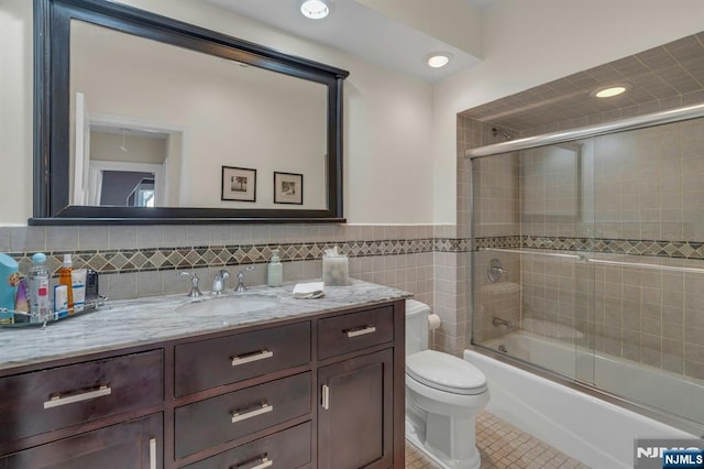 full bath with tile patterned flooring, tile walls, toilet, enclosed tub / shower combo, and vanity