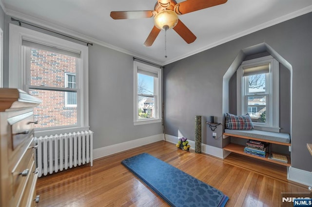 workout room featuring radiator, crown molding, baseboards, and hardwood / wood-style floors