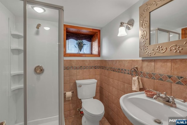 full bath with a wainscoted wall, toilet, a stall shower, a sink, and tile walls