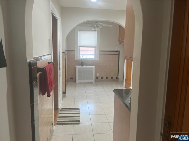 corridor with light tile patterned floors, arched walkways, tile walls, and wainscoting