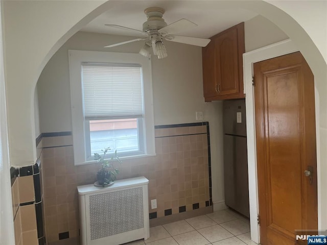 kitchen with light tile patterned floors, radiator, ceiling fan, freestanding refrigerator, and tile walls