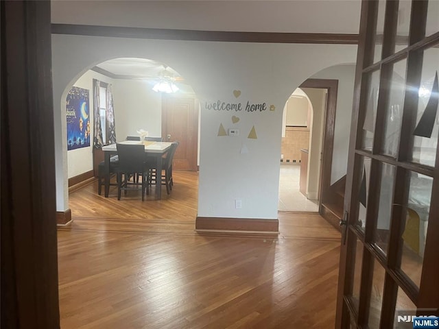 dining space featuring arched walkways, hardwood / wood-style floors, ornamental molding, and baseboards