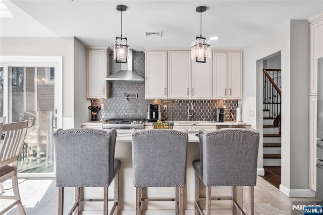 kitchen with decorative backsplash, a kitchen breakfast bar, light countertops, and wall chimney exhaust hood