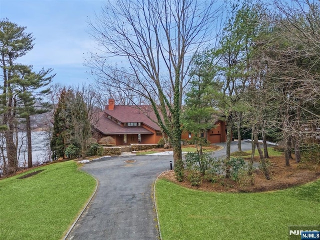 view of front of home featuring aphalt driveway, a front yard, and a chimney