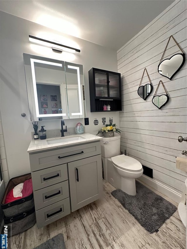 bathroom featuring wood walls, vanity, toilet, and wood finished floors