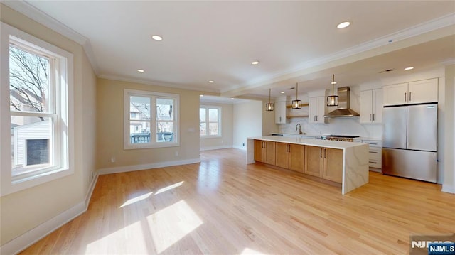 kitchen with light countertops, light wood-style flooring, ornamental molding, freestanding refrigerator, and wall chimney range hood