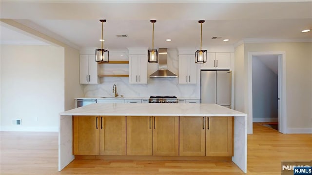 kitchen featuring visible vents, appliances with stainless steel finishes, a sink, wall chimney range hood, and a kitchen island