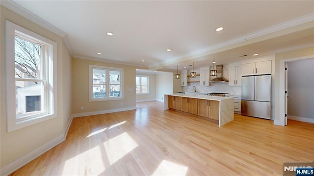 kitchen featuring light countertops, light wood-type flooring, stainless steel refrigerator, wall chimney exhaust hood, and crown molding