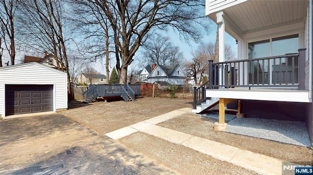 view of yard with driveway, a detached garage, fence, a wooden deck, and an outdoor structure