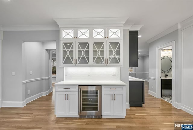 bar with light wood-style flooring, decorative backsplash, ornamental molding, a bar, and beverage cooler