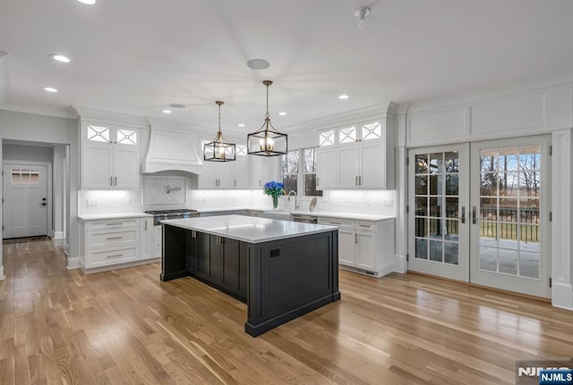 kitchen with light countertops, ornamental molding, custom exhaust hood, and white cabinets