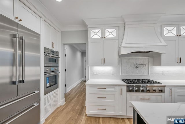 kitchen featuring premium range hood, appliances with stainless steel finishes, white cabinetry, and crown molding