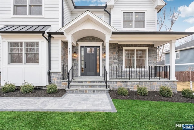 doorway to property with a porch, a lawn, a standing seam roof, metal roof, and stone siding