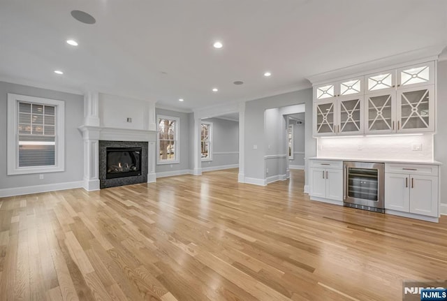 unfurnished living room featuring wine cooler, light wood-style floors, a glass covered fireplace, a bar, and baseboards