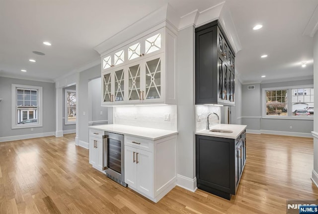 kitchen with beverage cooler, a sink, light countertops, ornamental molding, and glass insert cabinets