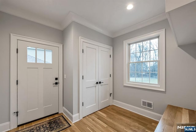 entrance foyer featuring ornamental molding, visible vents, light wood-style floors, and baseboards