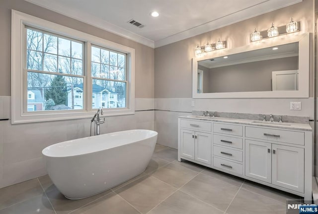 bathroom with a freestanding tub, a sink, visible vents, ornamental molding, and double vanity