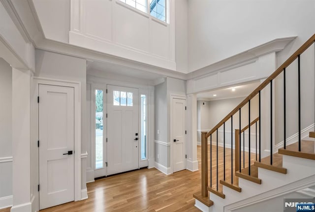 foyer featuring light wood-style floors, stairway, a towering ceiling, and baseboards