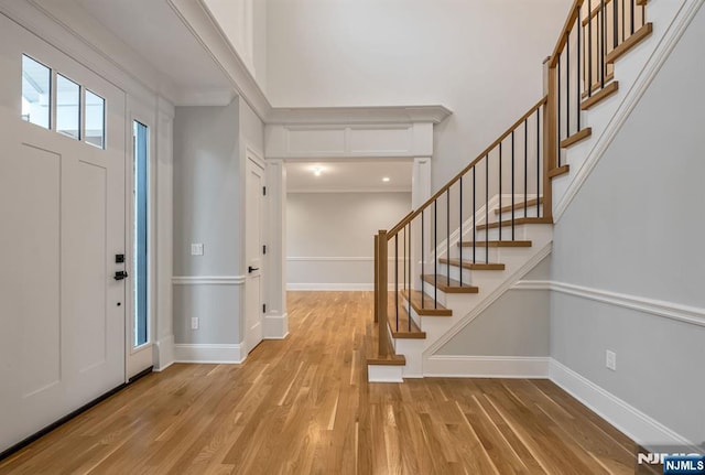 foyer featuring stairway, baseboards, a towering ceiling, and light wood finished floors