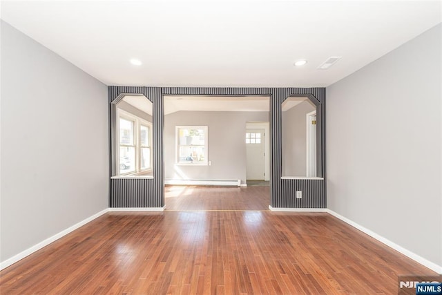 empty room featuring baseboards, a baseboard radiator, arched walkways, and wood finished floors