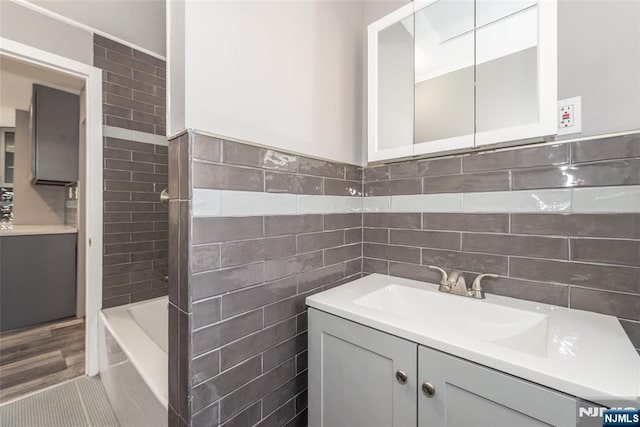 bathroom featuring a washtub, tile walls, and vanity