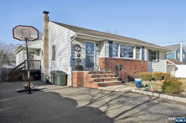 view of front of house with a shingled roof, a chimney, fence, and brick siding