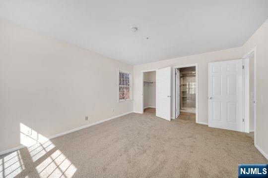 unfurnished bedroom with a walk in closet, a closet, connected bathroom, carpet flooring, and baseboards