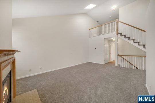 unfurnished living room featuring a glass covered fireplace, carpet flooring, and high vaulted ceiling