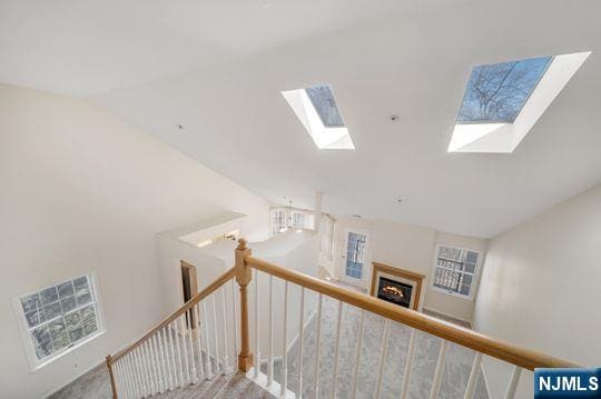 stairway with lofted ceiling with skylight and a warm lit fireplace