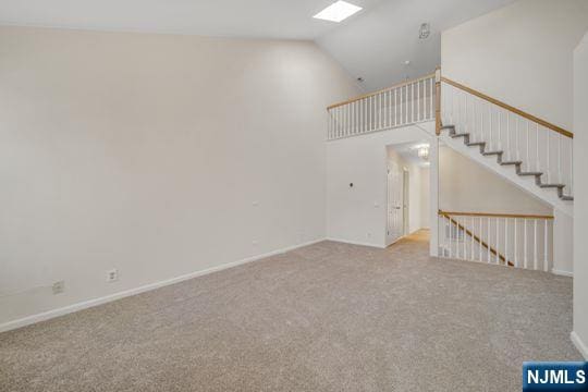 unfurnished living room with baseboards, stairway, high vaulted ceiling, and carpet