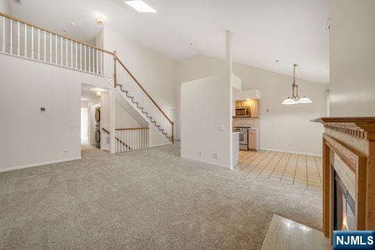 unfurnished living room with light colored carpet, a lit fireplace, and high vaulted ceiling