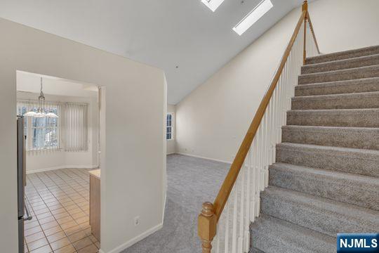 stairs with baseboards, carpet, a chandelier, a skylight, and tile patterned floors