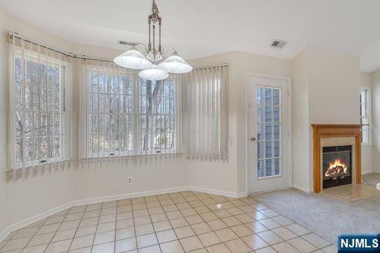 unfurnished dining area with tile patterned flooring, visible vents, baseboards, a lit fireplace, and carpet flooring