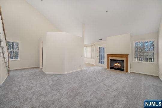 unfurnished living room with carpet, baseboards, a lit fireplace, and high vaulted ceiling