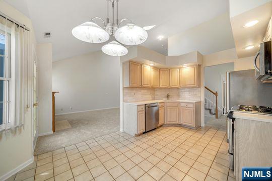 kitchen with backsplash, light brown cabinetry, light countertops, light carpet, and stainless steel appliances