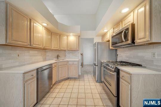 kitchen with light brown cabinets, appliances with stainless steel finishes, light countertops, and a sink