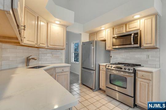 kitchen featuring light tile patterned floors, a sink, stainless steel appliances, light countertops, and backsplash