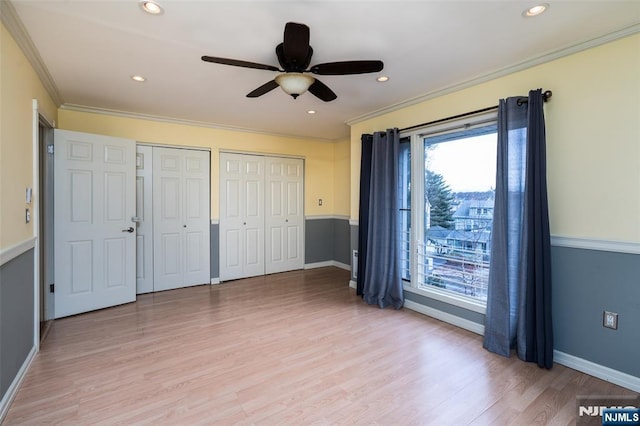 unfurnished bedroom featuring light wood finished floors, crown molding, and multiple closets