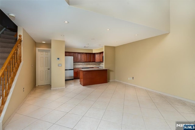 kitchen with light tile patterned floors, open floor plan, freestanding refrigerator, a peninsula, and backsplash