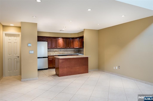 kitchen featuring light tile patterned floors, baseboards, decorative backsplash, freestanding refrigerator, and a peninsula