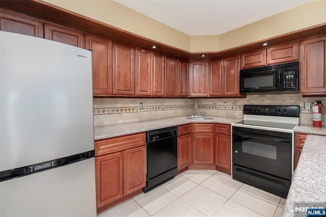 kitchen featuring light tile patterned floors, a sink, brown cabinets, black appliances, and tasteful backsplash