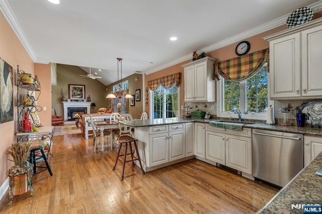 kitchen featuring open floor plan, a lit fireplace, light wood-style flooring, stainless steel dishwasher, and a sink