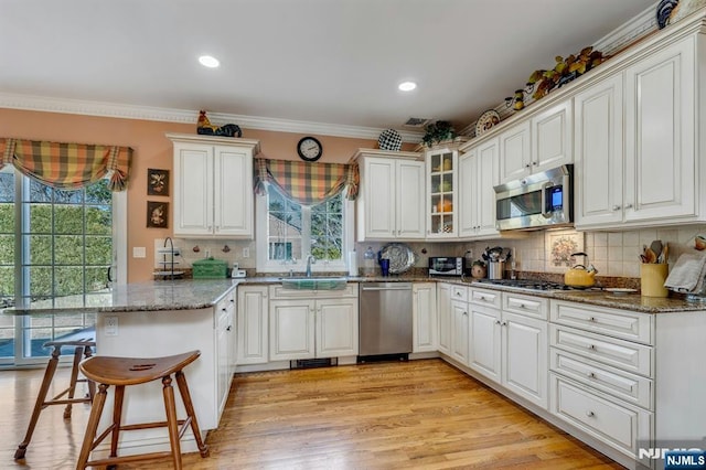 kitchen with ornamental molding, a peninsula, a kitchen breakfast bar, stainless steel appliances, and a sink