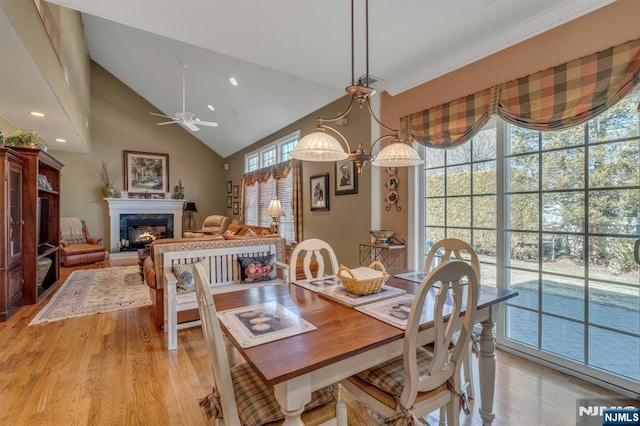 dining room featuring light wood-type flooring, high vaulted ceiling, a ceiling fan, a warm lit fireplace, and recessed lighting