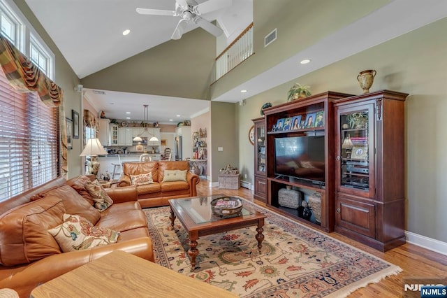 living area featuring visible vents, a healthy amount of sunlight, light wood-style floors, and a towering ceiling