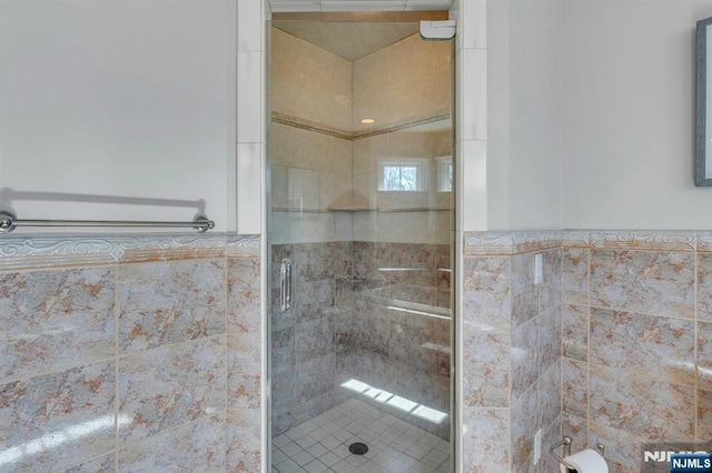 full bath with a shower stall, tile walls, and wainscoting